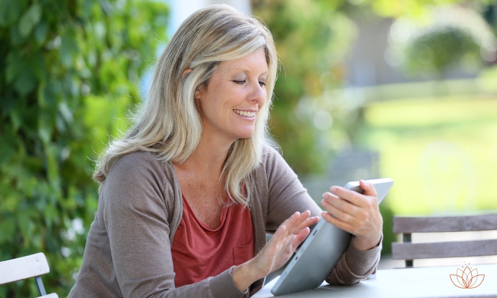 Achtsamkeitstrainer-Online-Ausbildung: Frau sitzt mit iPad im Garten und lernt.